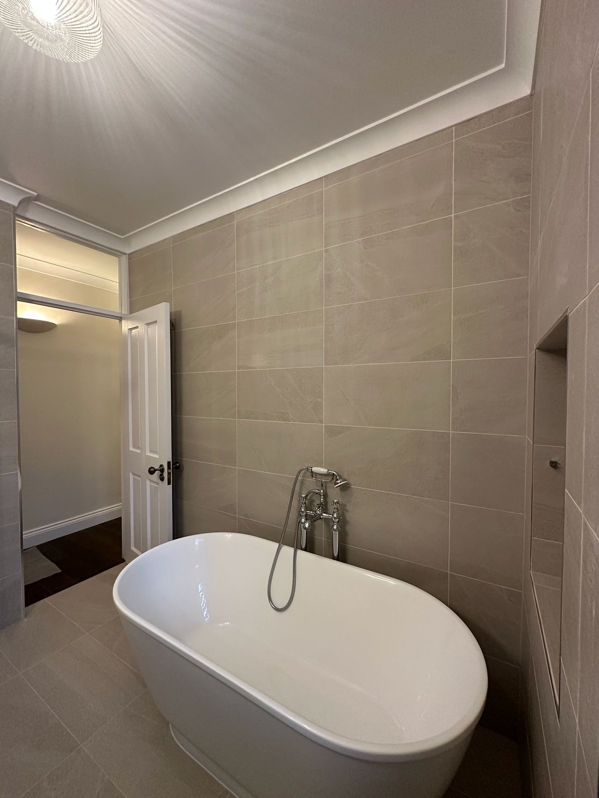 Freestanding bath with chrome telephone tap against large-format stone tiling, Kennington