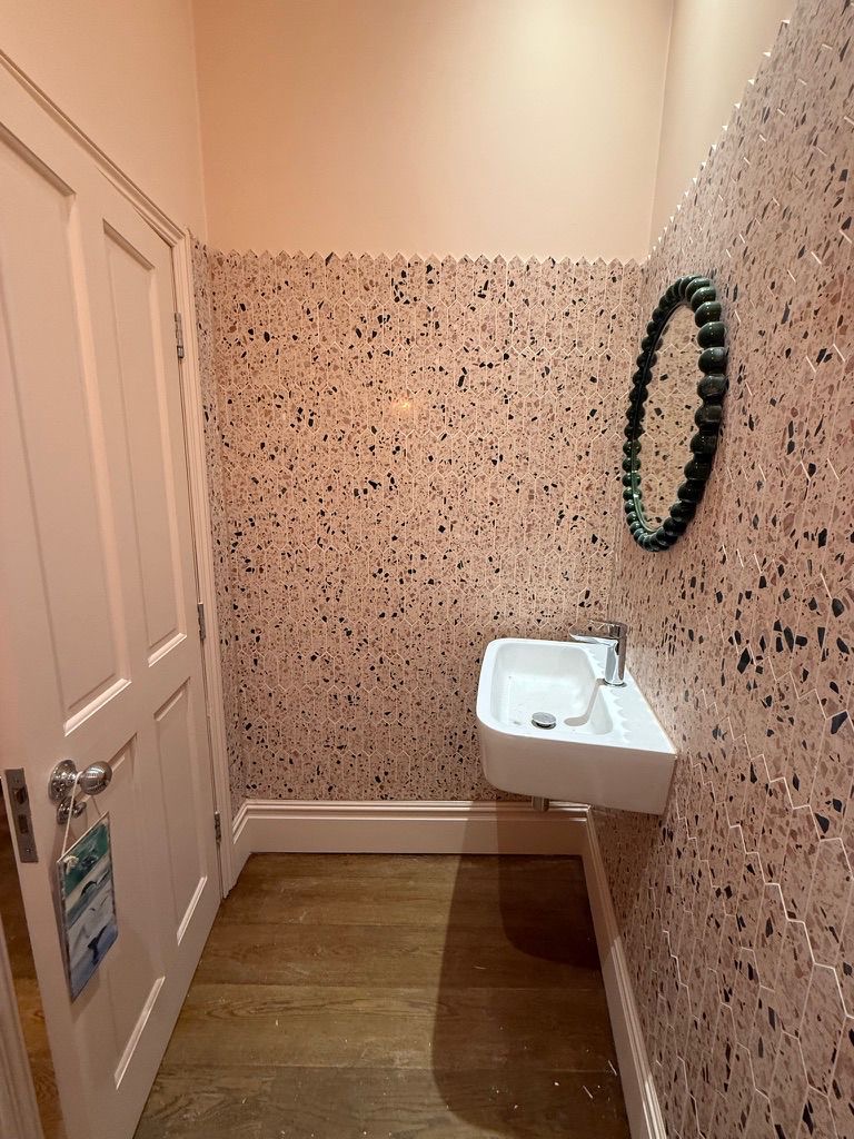 Picket-cut pink terrazzo walls with beaded emerald mirror and small wall-hung basin, Fulham cloakroom