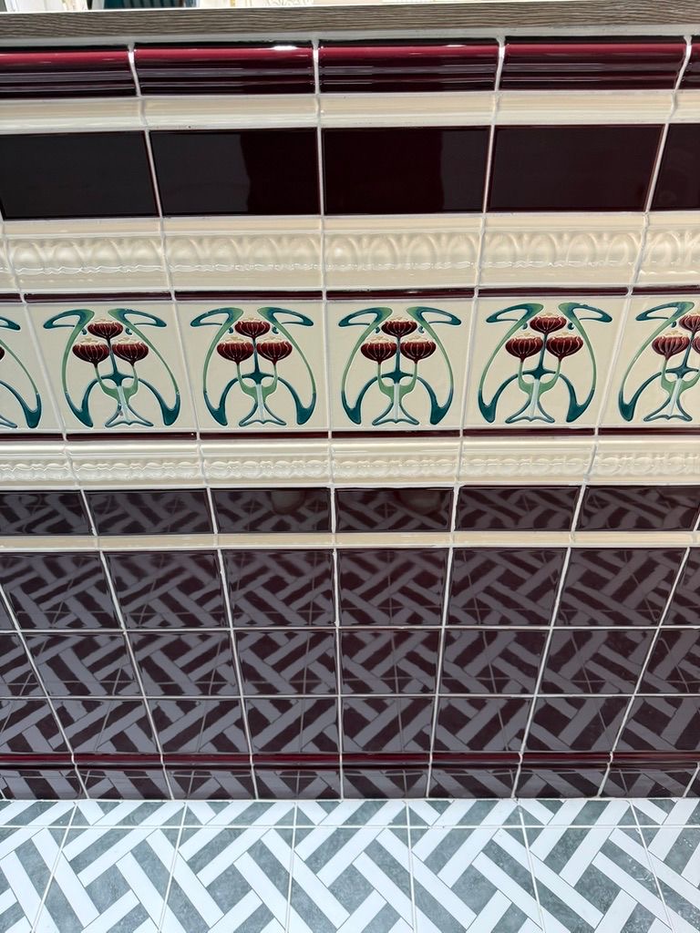 Close-up of Art Nouveau tulip border, gloss burgundy metro tiles and basket-weave mosaic flooring at Clay and Rock