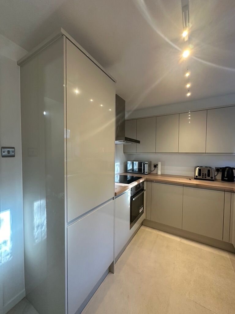 Cream gloss handleless kitchen with timber worktop and garden window, Croydon renovation by Atmosphere Interiors